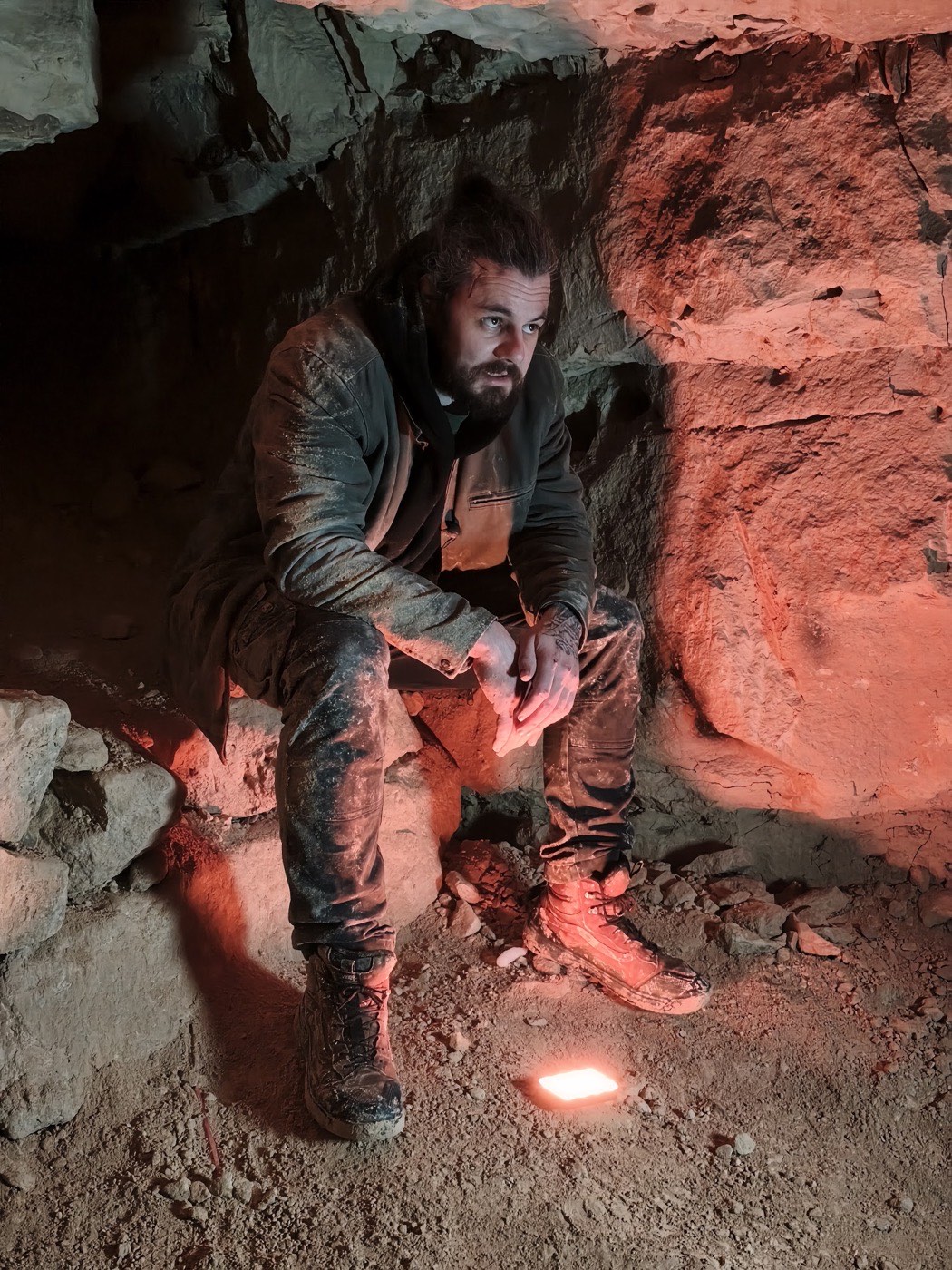 Un homme blessé, éclairé de rouge, assis dans une grotte.