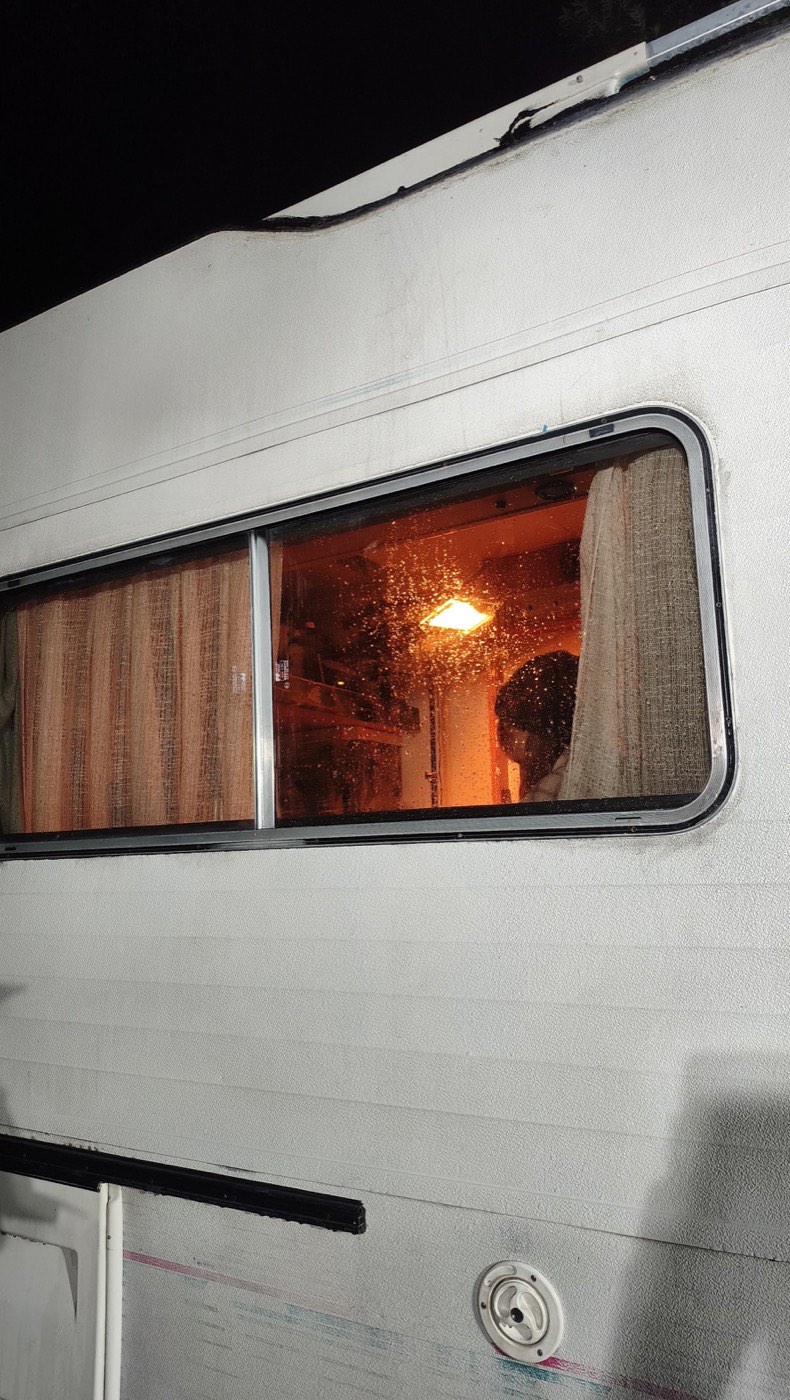 Fenêtre de camping-car éclairée en orange, la nuit.